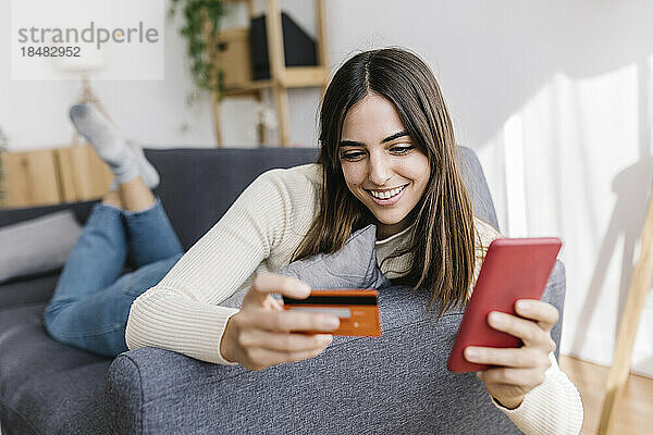 Glückliche Frau mit Kreditkarte  die zu Hause auf dem Smartphone einkauft