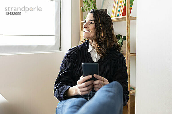 Lächelnde Geschäftsfrau sitzt mit Smartphone im Büro