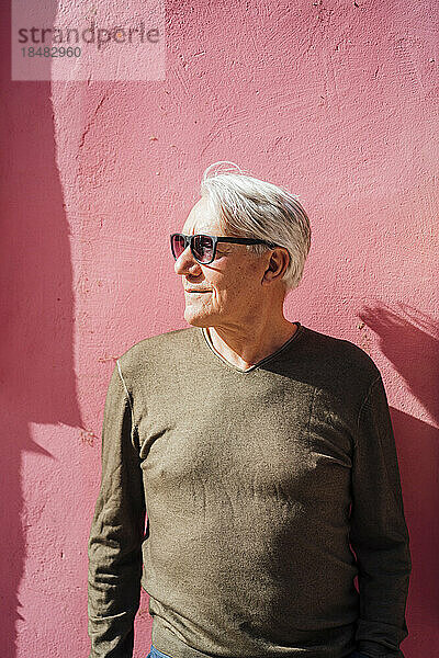 Lächelnder älterer Mann mit Sonnenbrille steht vor rosa Wand