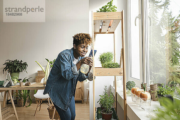 Lächelnde Frau vloggt und sprüht Pflanzen auf dem heimischen Regal