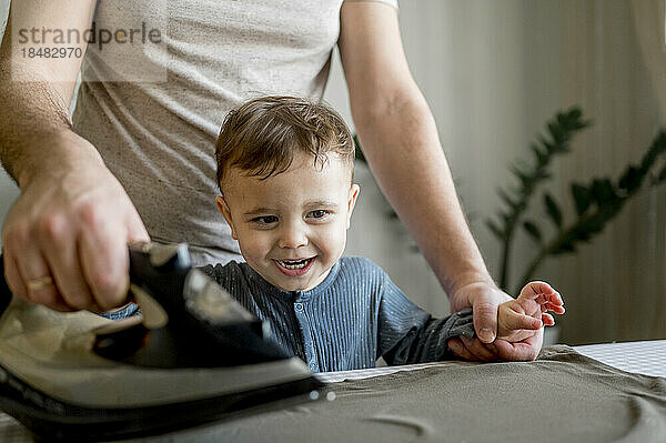 Glücklicher Junge genießt es  zu Hause mit seinem Vater Kleidung zu bügeln