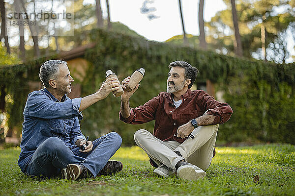 Ältere Freunde sitzen im Gras und klirren mit Mehrwegflaschen