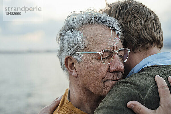 Lächelnder älterer Mann mit grauem Haar  der seinen Sohn umarmt