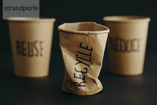Crushed reusable cup with recycle text written on it against black background