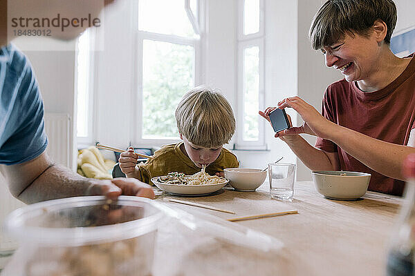 Glückliche Frau fotografiert Sohn beim Essen zu Hause