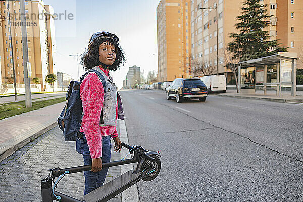 Lächelnde Frau mit Elektroroller steht auf der Straße