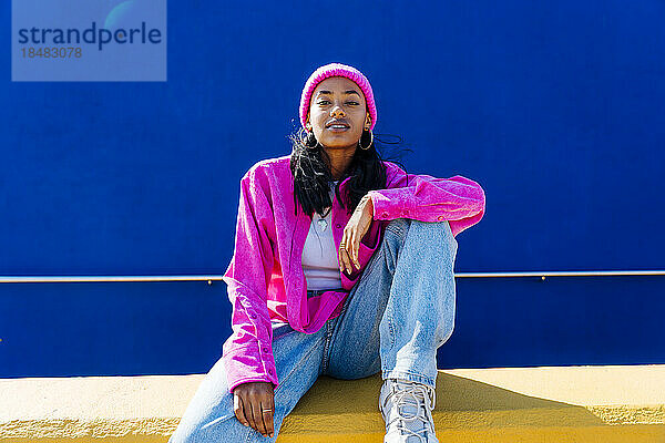 Junge Frau in rosa Jacke sitzt an der Wand