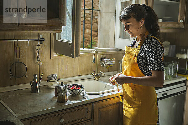 Junge Frau in gelber Schürze steht an der Küchentheke