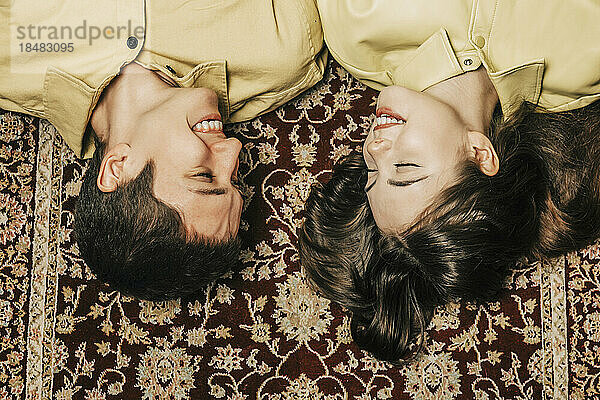 Happy teenage couple lying down on carpet at home