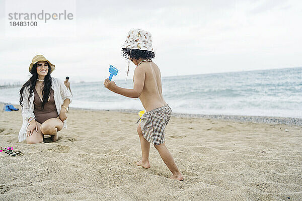 Boy wearing hat running towards mother at beach