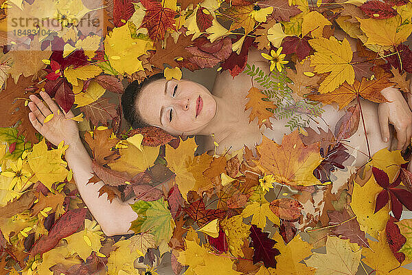 Frau entspannt sich mit Herbstblättern in der Badewanne