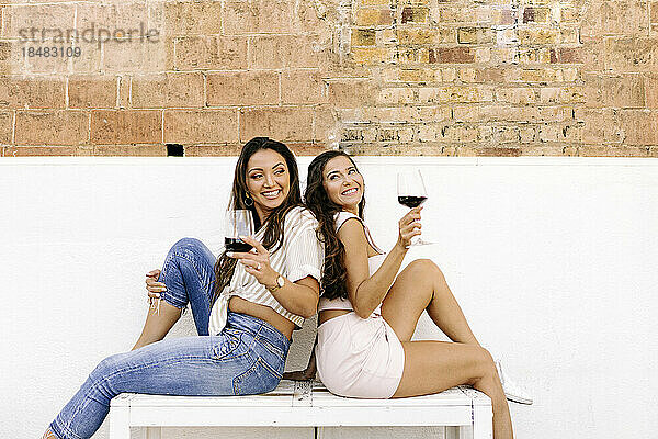 Fröhliche Freunde sitzen mit Weingläsern auf einer Bank