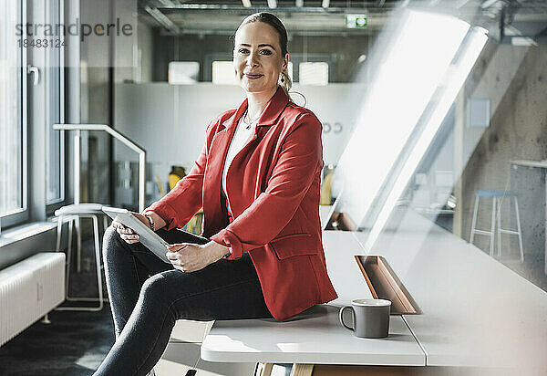 Selbstbewusste Geschäftsfrau mit Tablet-PC sitzt am Schreibtisch im Büro