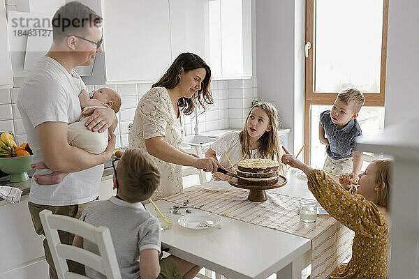 Mutter schneidet Kuchen an  während Kinder am Tisch in der Küche sitzen