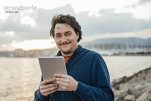 Mann mit Tablet-PC steht vor dem Meer