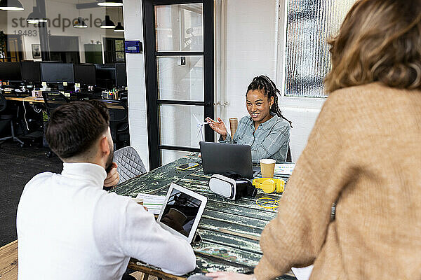 Lächelnde Geschäftsfrau zeigt Kollegen im Büro das Modell einer Windkraftanlage