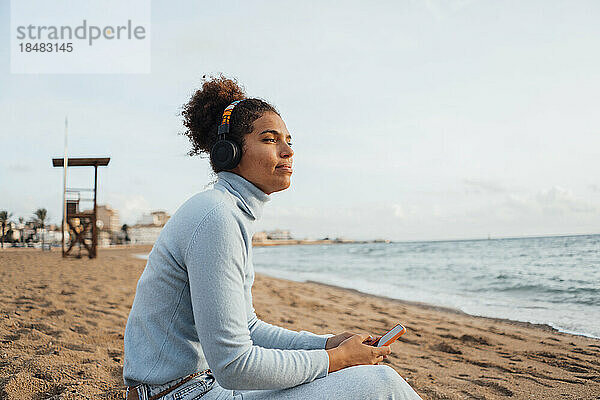 Contemplative young woman sitting with smart phone at beach