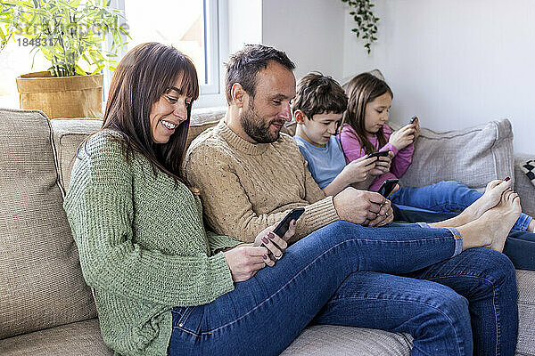 Glücklicher Mann und Frau mit Kindern  die zu Hause ihr Smartphone nutzen