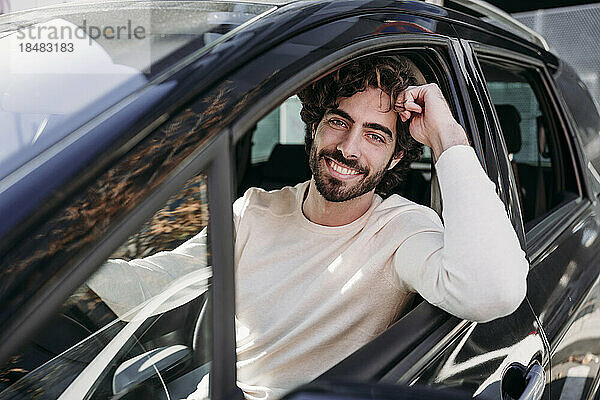 Lächelnder junger Mann mit Bart lehnt an Autofenster