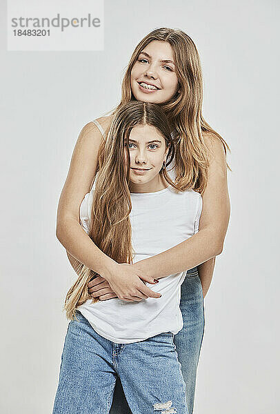 Smiling sisters standing together against white background