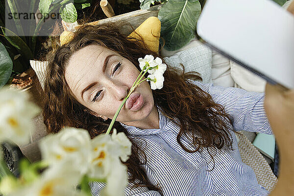 Frau macht ein Selfie mit einer Blume auf den Lippen