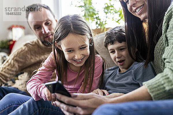 Glückliches Mädchen  das Smartphone benutzt  während die Familie zu Hause auf dem Sofa sitzt