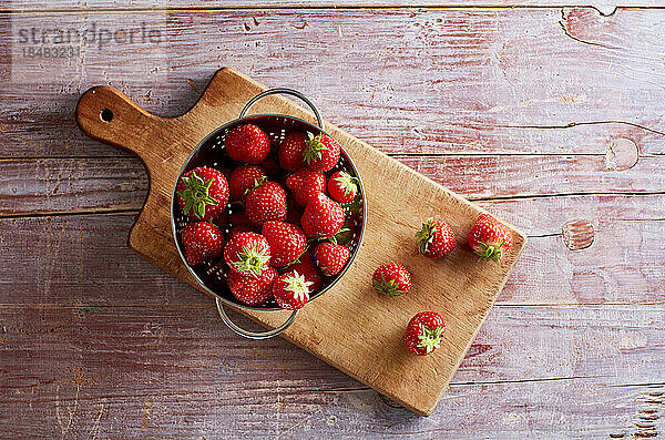 Colander with fresh strawberries lying on cutting board