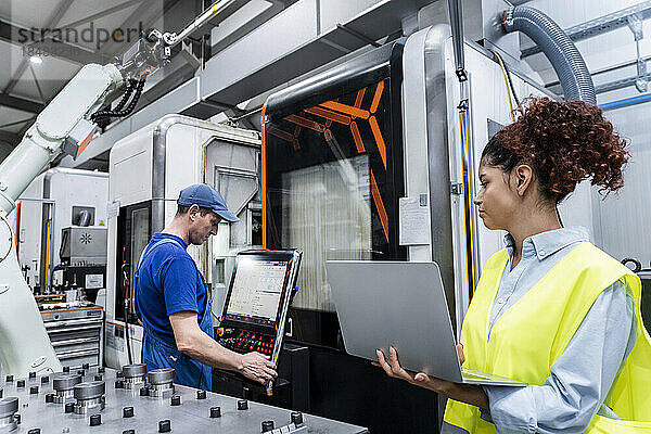 Ingenieur hält Laptop in der Hand und steht Kollegen in der Industrie zur Seite