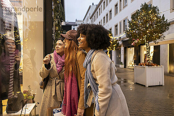 Fröhliche junge Freunde genießen gemeinsam einen Schaufensterbummel vor dem Laden