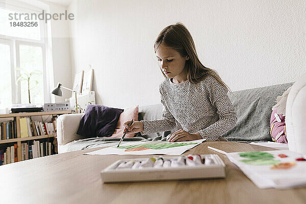 Girl doing painting with paintbrush on paper at home