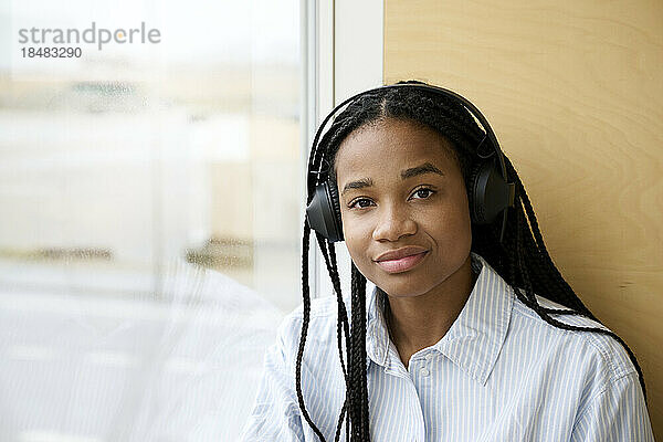 Lächelnde junge Frau mit geflochtenem Haar und kabellosen Kopfhörern