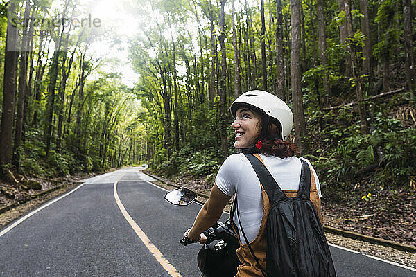 Glückliche Frau mit Helm  die auf der Straße Motorrad fährt