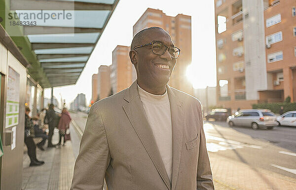 Glücklicher Geschäftsmann mit Brille an der Straßenbahnhaltestelle in der Stadt