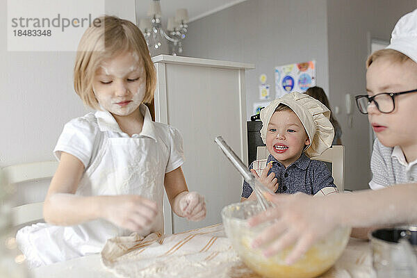 Kinder bereiten in der Küche Teig mit Mehl zu