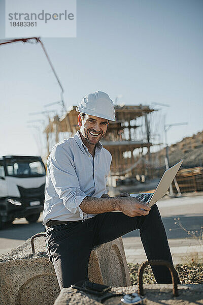 Glücklicher reifer Architekt mit Laptop auf der Baustelle
