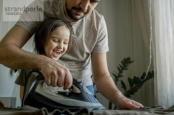 Glücklicher Junge hilft Vater beim Bügeln von Kleidung zu Hause