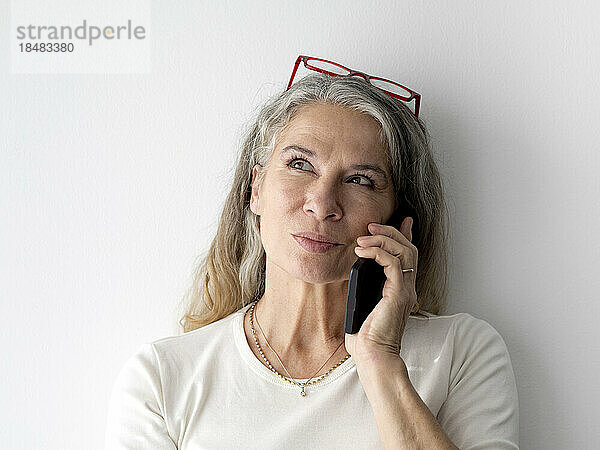 Nachdenkliche ältere Geschäftsfrau  die vor der Wand mit dem Smartphone spricht