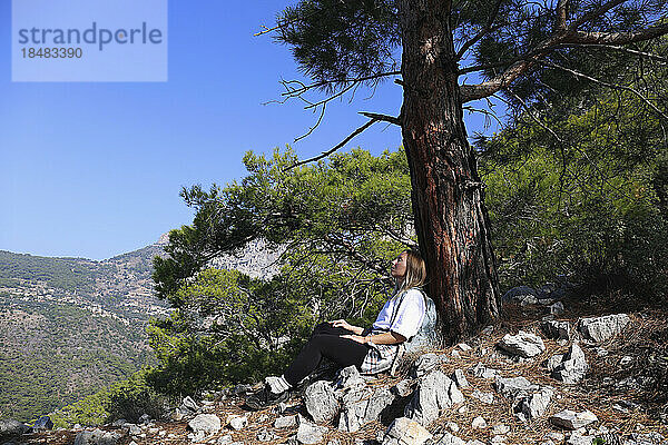 Woman leaning on tree trunk taking break from hike