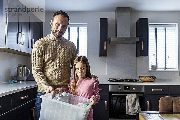 Lächelnder Vater mit Mädchen  das zu Hause Plastikflaschen in der Küche recycelt