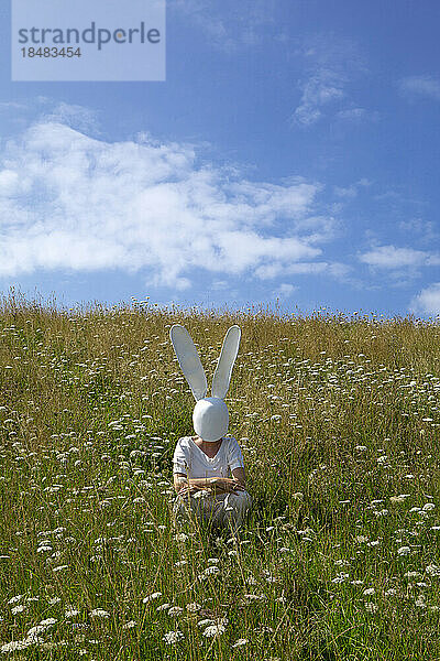 Woman wearing rabbit mask crouching in field