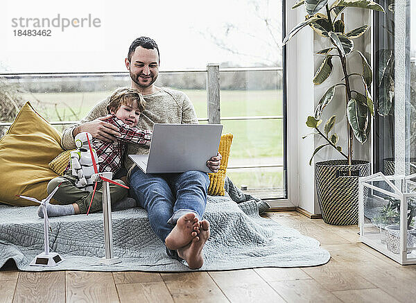 Vater und Sohn schauen auf den Laptop und sitzen auf dem Sofa mit Windkraftanlagen