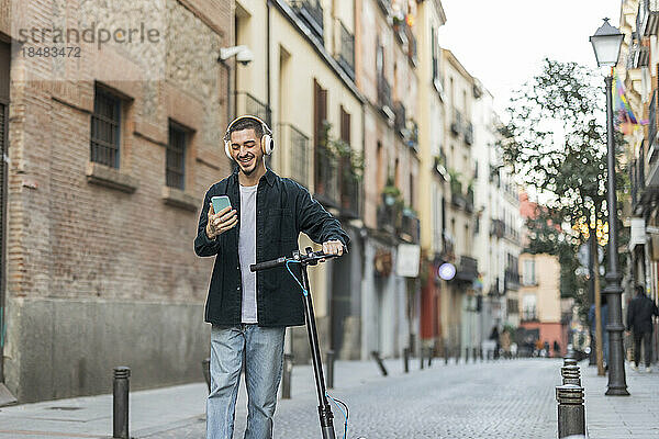 Glücklicher Mann benutzt Smartphone und läuft mit Elektroroller auf der Straße