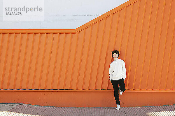 Man standing in front of orange wall on footpath