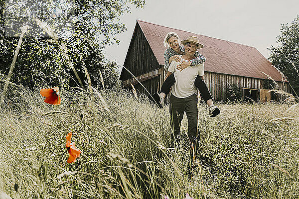 Happy man piggybacking woman in front of barn
