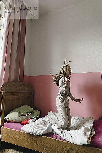 Fröhliches Mädchen  das Spaß beim Springen auf dem Bett im Schlafzimmer hat