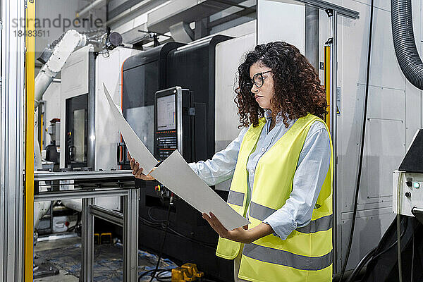 Junger Ingenieur untersucht Baupläne  die in der Industrie an einer Maschine stehen