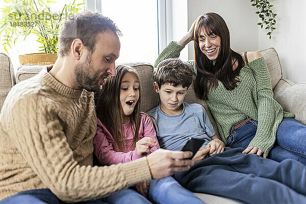 Glückliche Familie nutzt Smartphone auf dem Sofa zu Hause