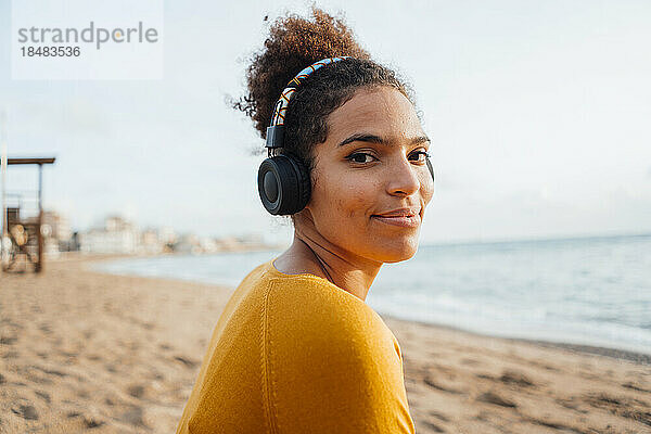 Lächelnde junge Frau mit Kopfhörern  die am Strand Musik hört