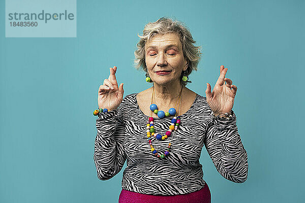 Woman crossing fingers with eyes closed against turquoise background