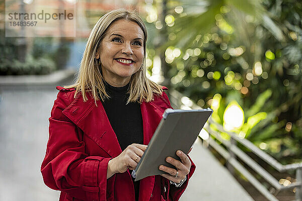 Glückliche reife Frau mit Tablet-PC steht auf Fußweg